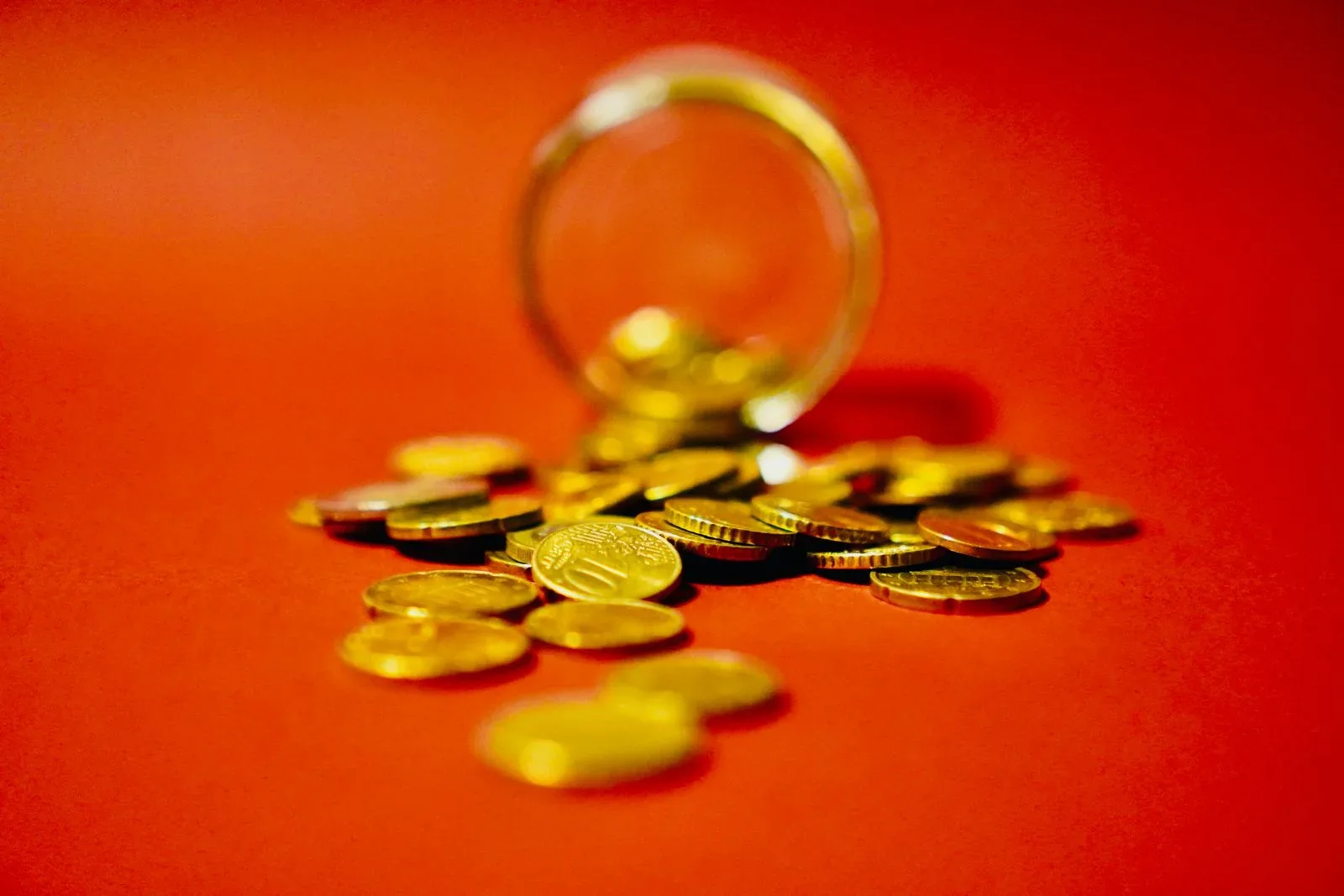 Gold-colored coins spilling from a glass on a red background