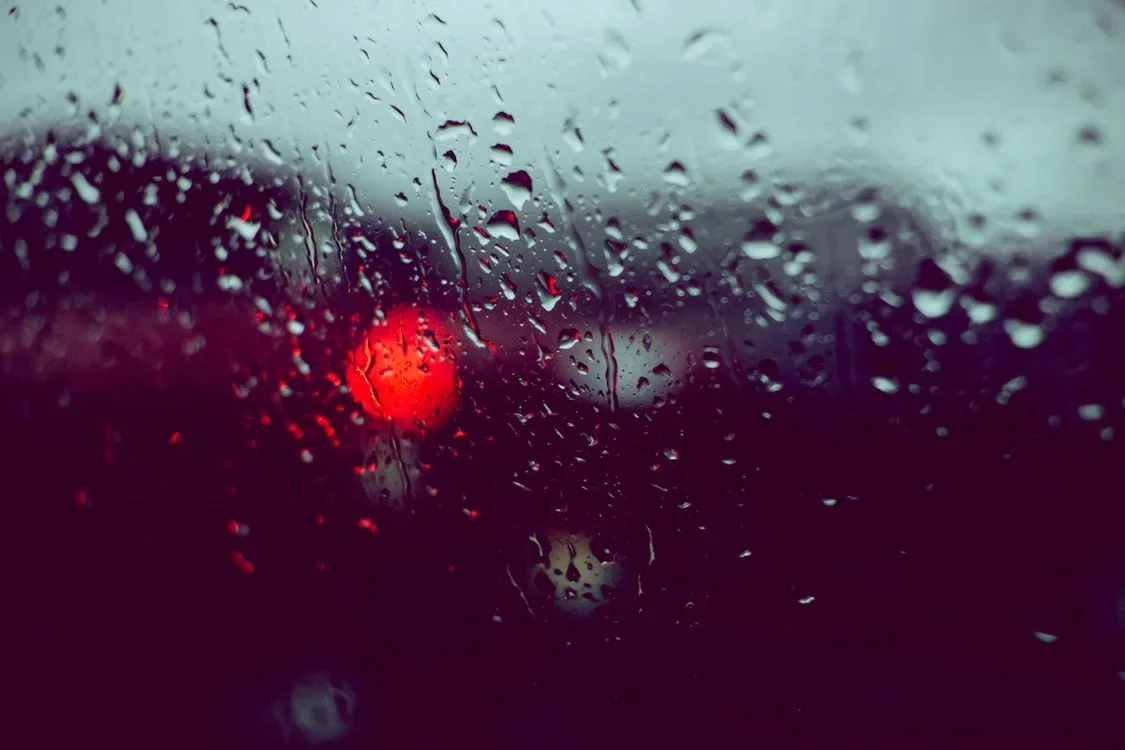 Raindrops on a car window with blurred lights beyond