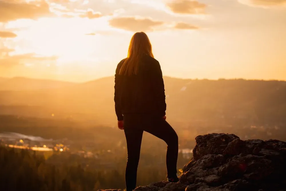 A woman standing on a rock at sunrise, a calm and steady pose