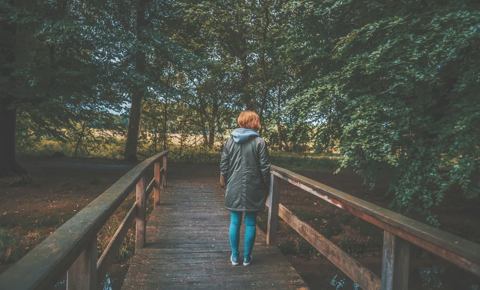 A person standing on a wooden footbridge as a symbol of transition