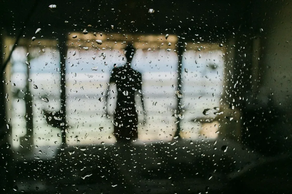 A man standing behind a window covered in raindrops