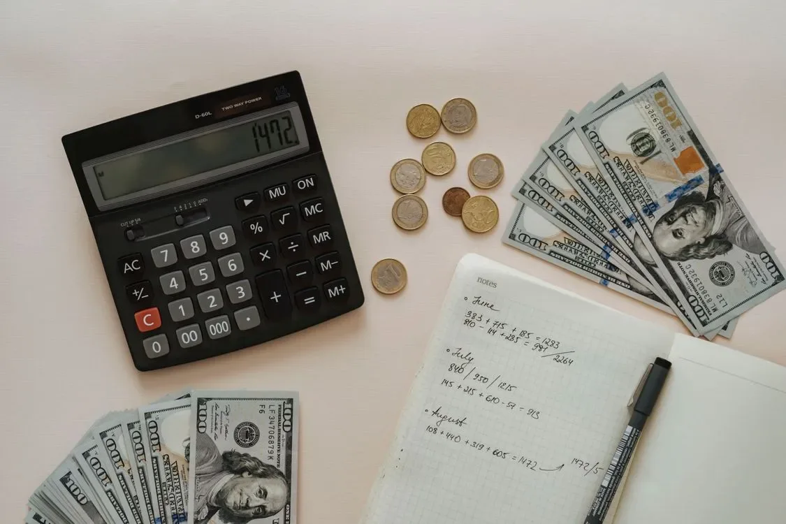 A calculator, cash and a notebook arranged on a desk