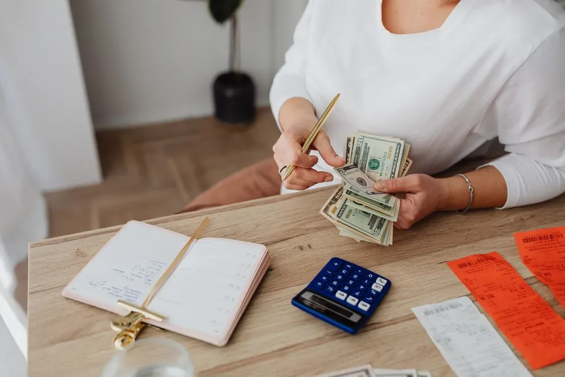 A person counting cash with a notebook beside them