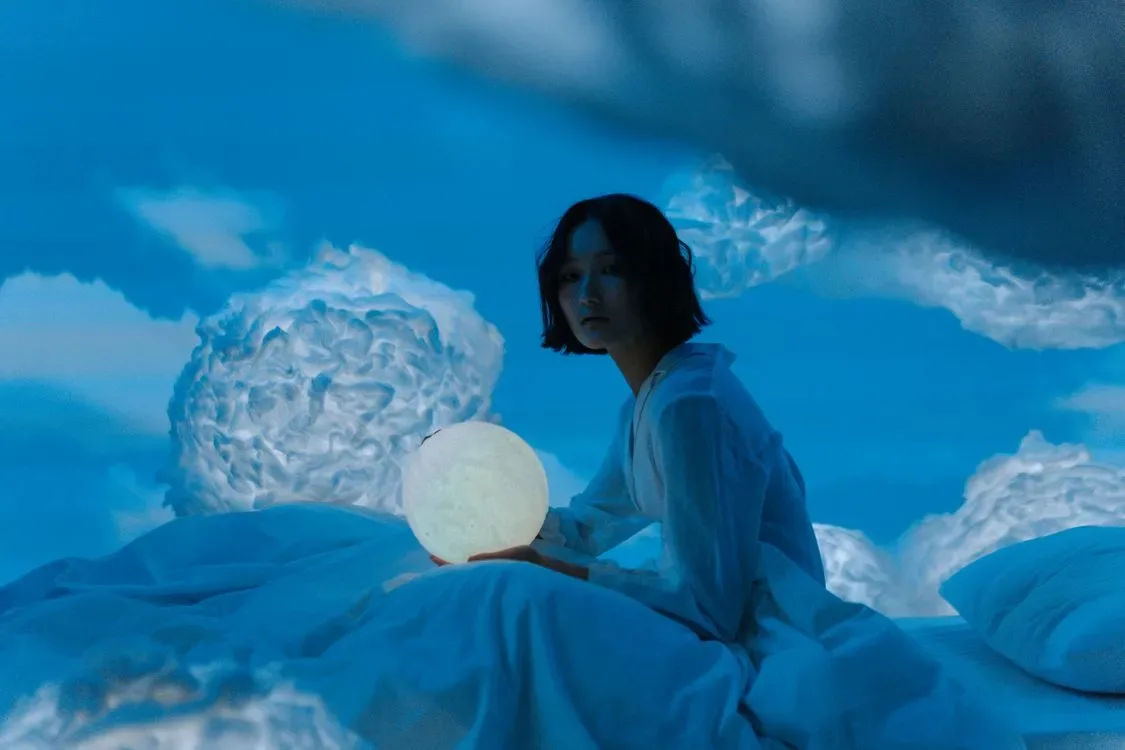 A woman sitting on a bed holding a glowing moon lamp at night