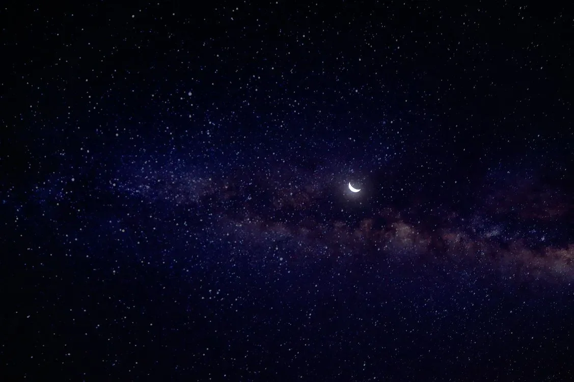 A clear night sky full of stars with a crescent moon