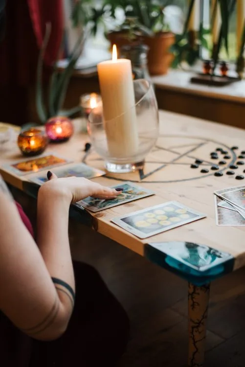 A hand resting near tarot cards and candles on a table