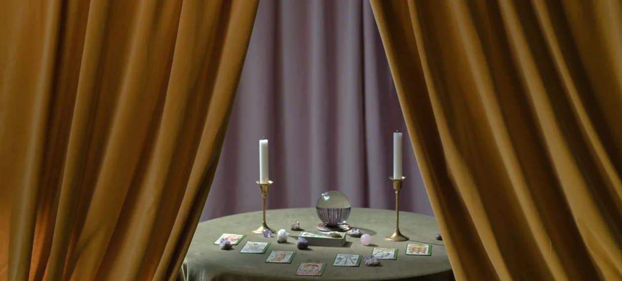 A curtained tarot table with cards, a candle and a crystal ball