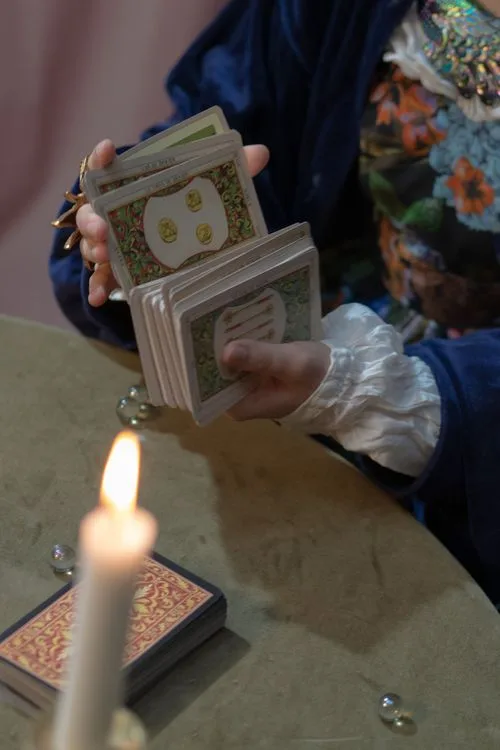 Hands holding a tarot deck beside a lit candle