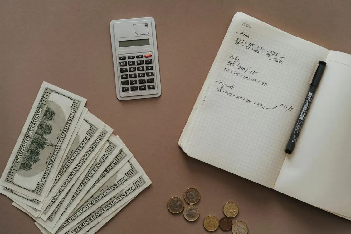 A notebook, calculator and cash arranged for reviewing everyday finances