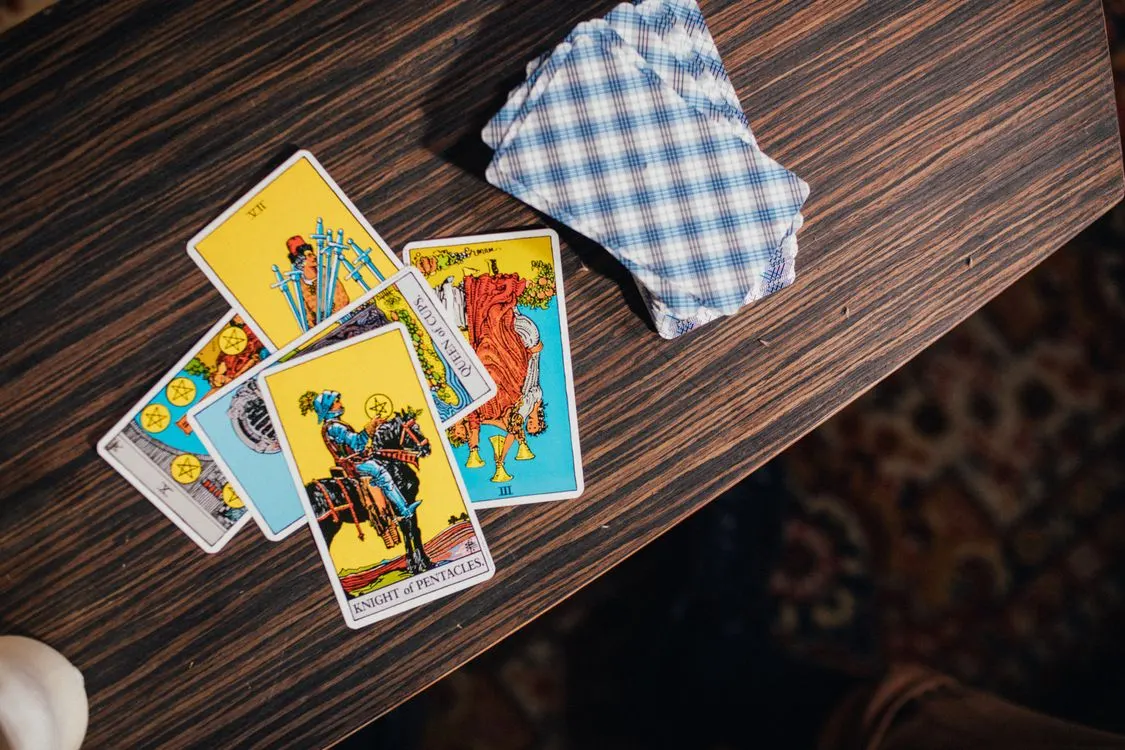 Tarot cards spread across a wooden table beside a face-down deck